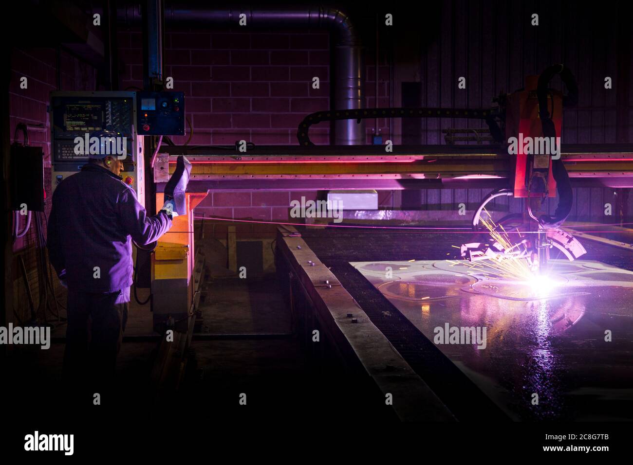 Uomo che lavora in una fabbrica d'acciaio, che opera una saldatrice computerizzata. Foto Stock