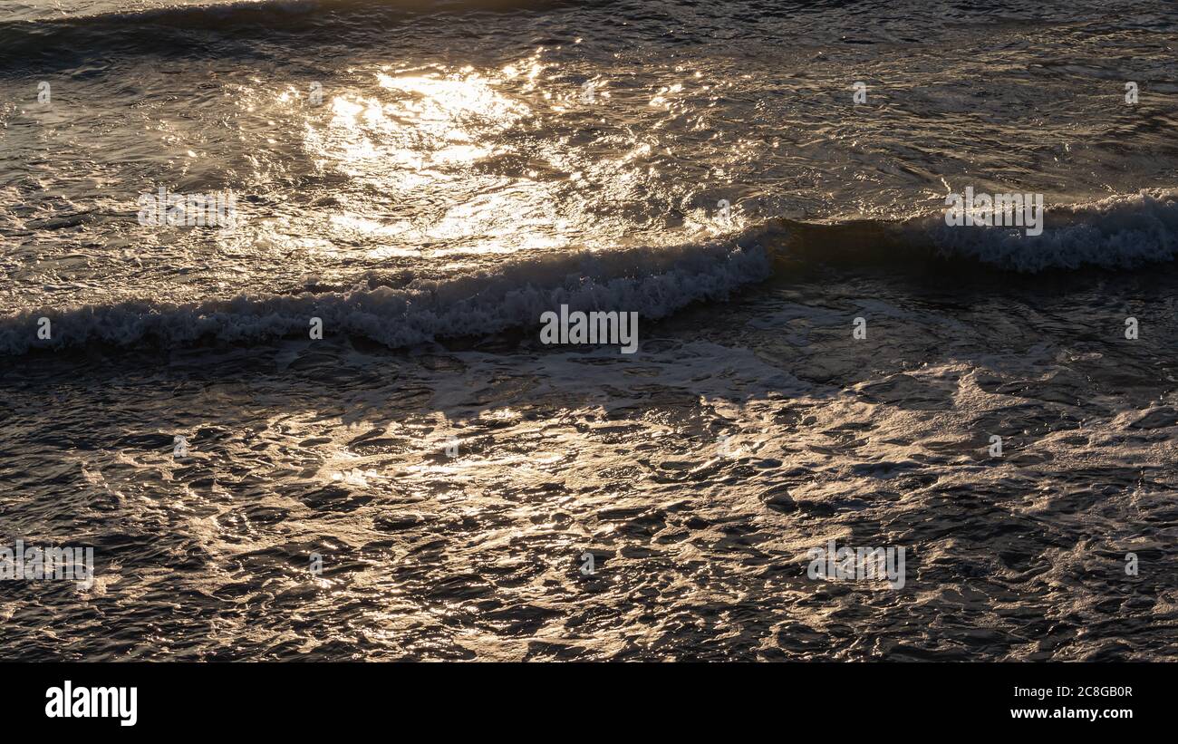 Estate mare, onde di schiuma che si precipitano verso la riva, i raggi luminosi del sole che si riflette sulla superficie del mare. Vista ravvicinata dalla scogliera. Foto Stock