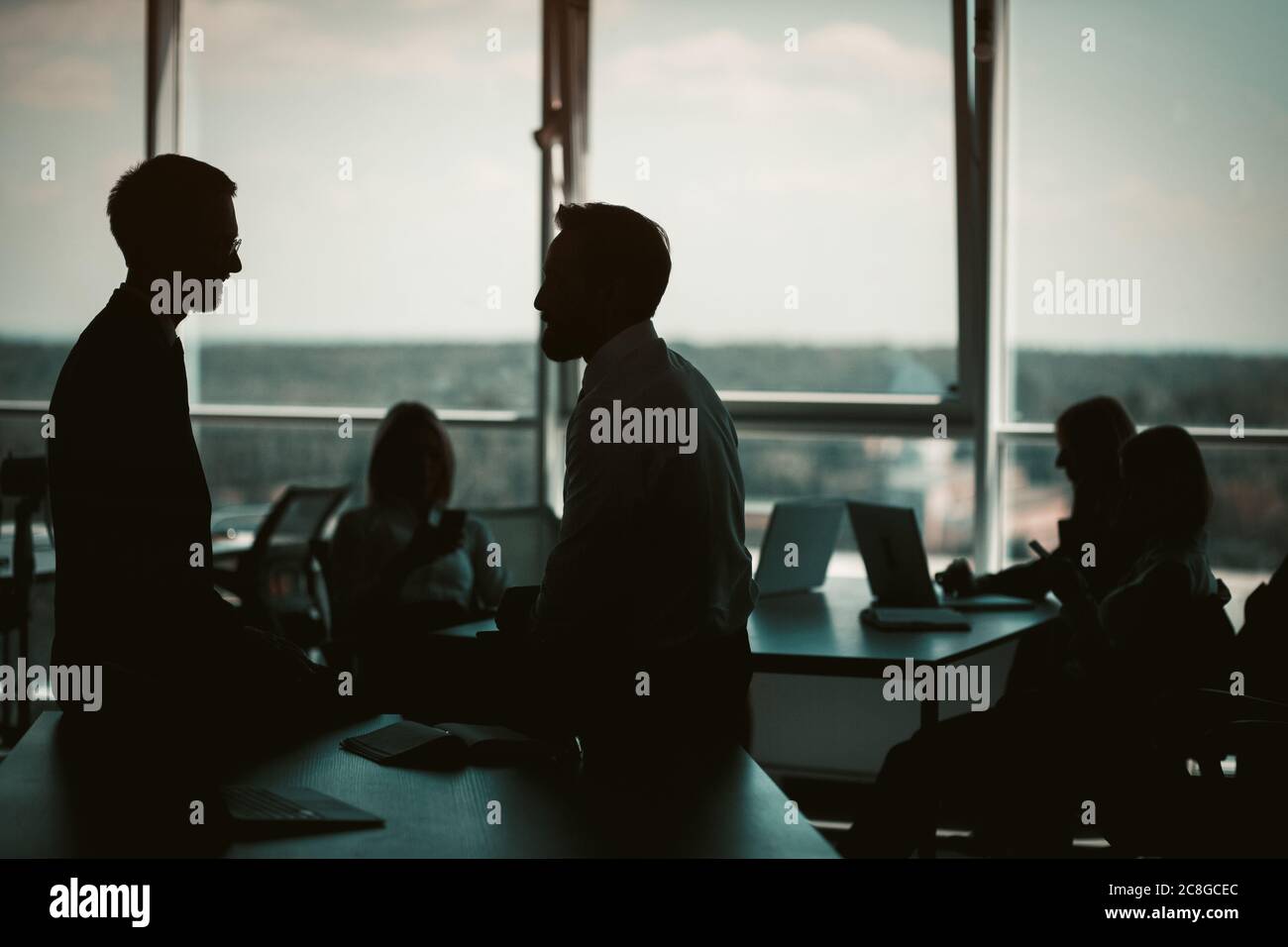 Silhouettes di uomini d'affari hanno discussione in interni di ufficio con le finestre enormi. Concetto di lavoro di squadra. Immagine colorata Foto Stock