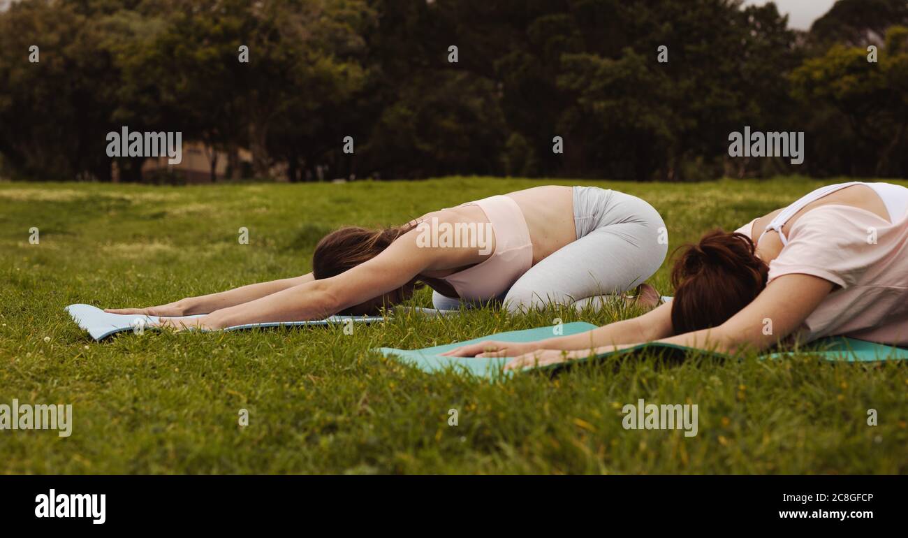 Due donne che si allenano yoga in un parco. Le donne praticano la posa del bambino mentre fanno yoga nel parco. Foto Stock