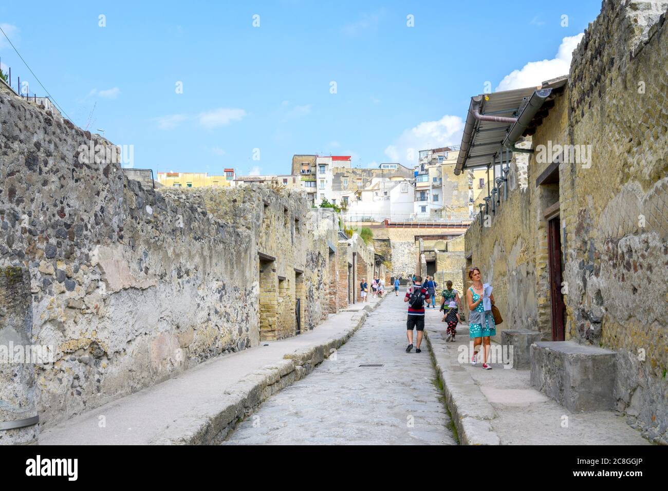 Si cammina lungo una strada tra edifici nella città romana di Ercolano, parzialmente distrutta dall'eruzione del Vesuvio nel 79 d.C. Foto Stock