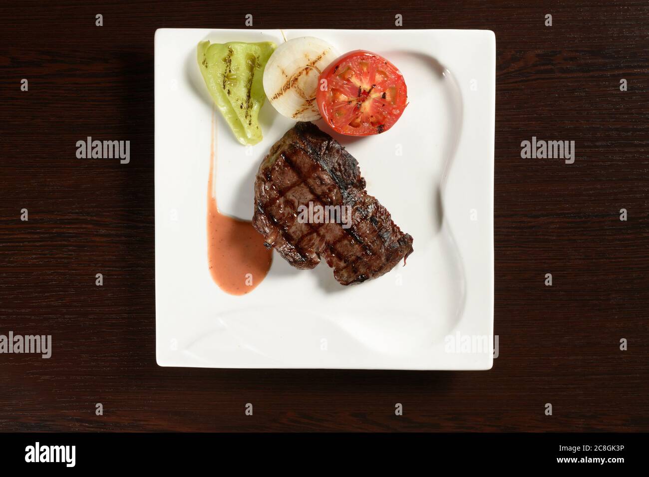 Carne arrosto di manzo marmoreo con verdure grigliate di pomodoro, cipolla e peperone su un piatto quadrato su un tavolo di legno. Vista dall'alto. Foto per Foto Stock