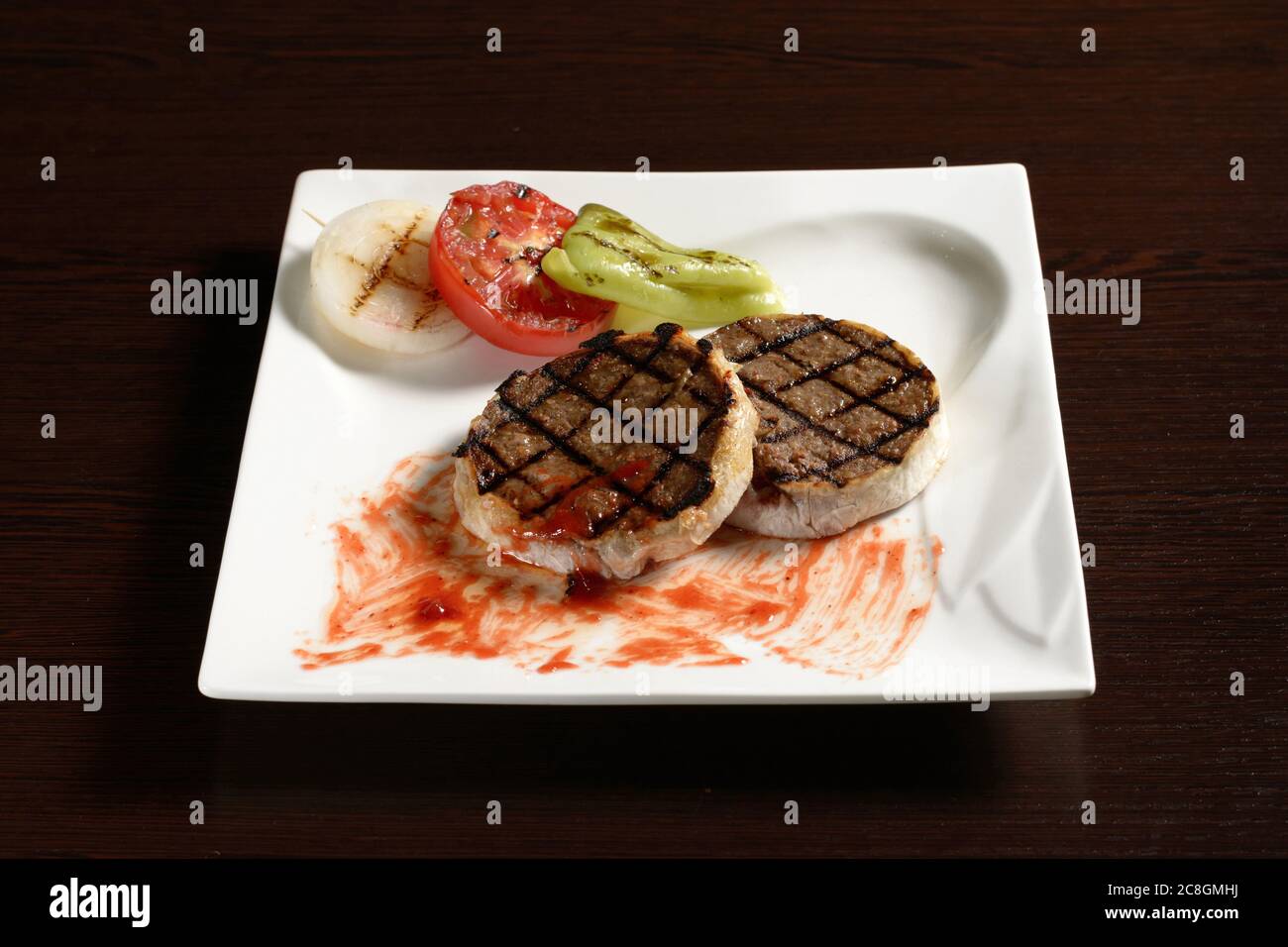 Filetto di manzo arrosto di bistecca con verdure grigliate di pomodoro, cipolla e peperone su un piatto quadrato su un tavolo di legno. Foto per la restaura Foto Stock