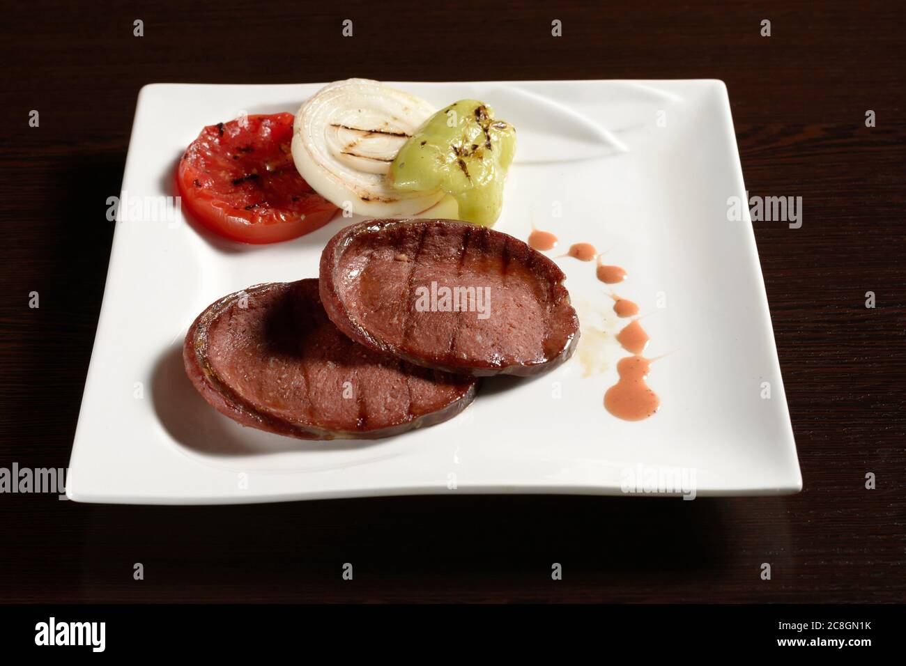 Fette di salsiccia di manzo alla griglia con verdure fritte di pomodoro, cipolla e peperone su un piatto quadrato su un tavolo di legno. Foto per ristorante e c Foto Stock