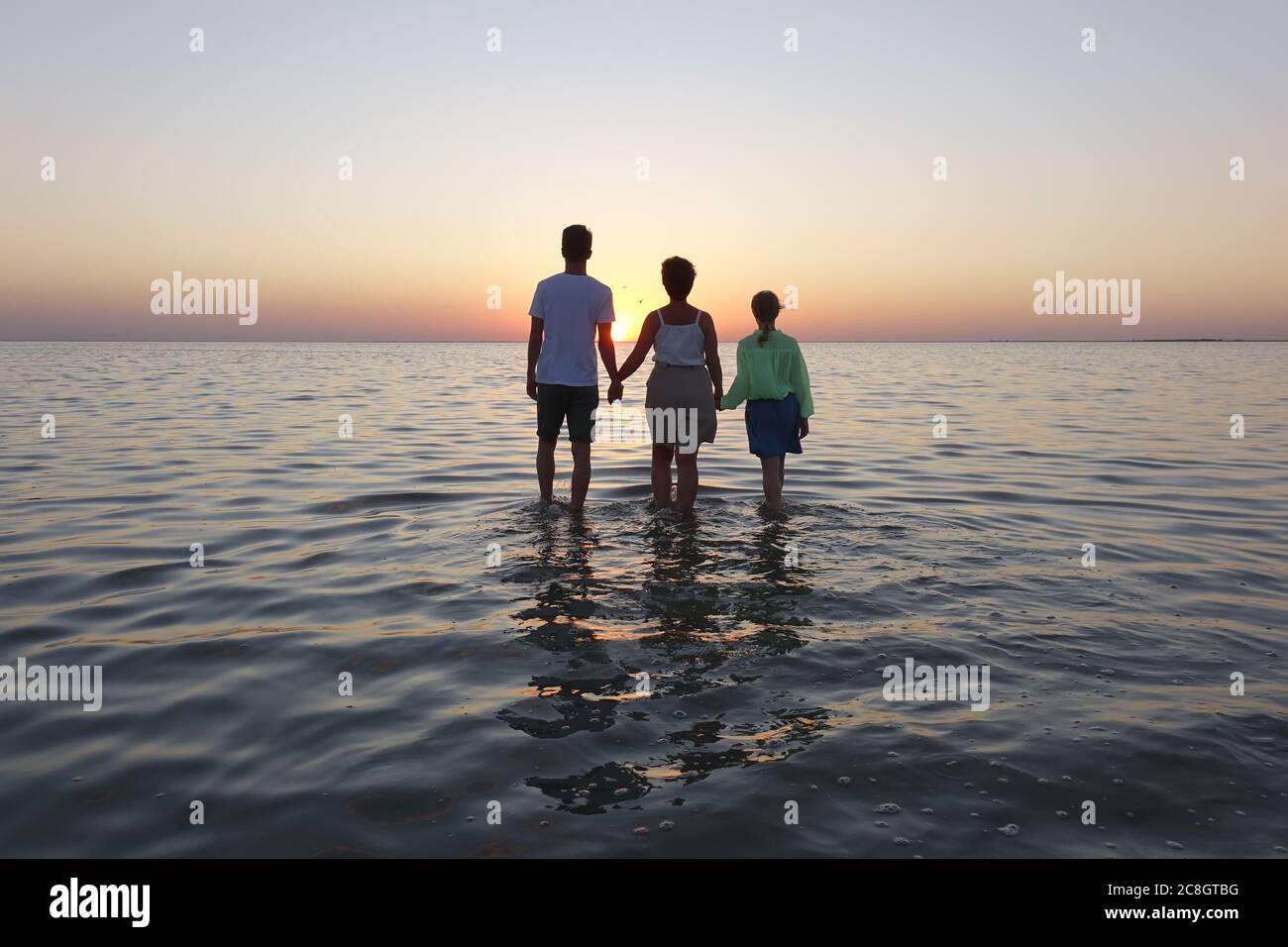 la famiglia cammina sull'acqua al tramonto Foto Stock