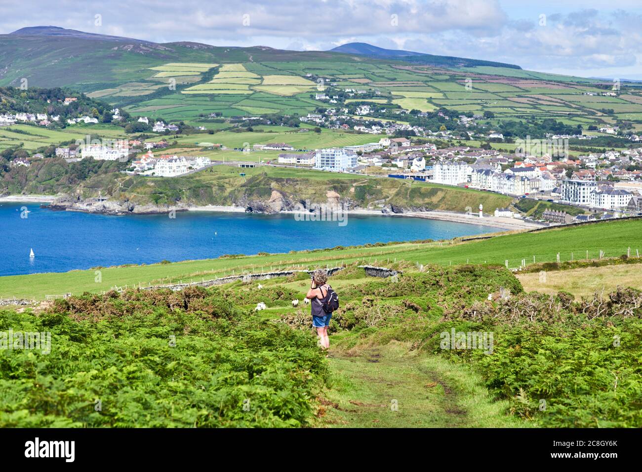 Donna che cammina su un sentiero alto sopra Port Erin si ferma per scattare una foto Foto Stock