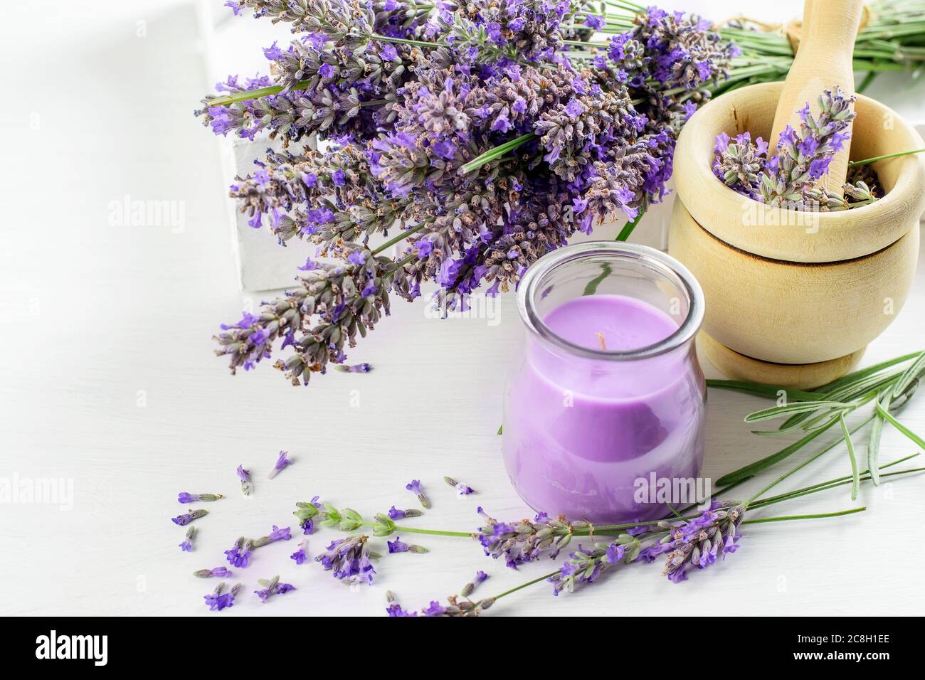 Bouquet di fiori di lavanda, mortaio di legno con pestello e candela di lavanda sul primo piano di sfondo bianco. Aroma di erbe concetto. Foto Stock