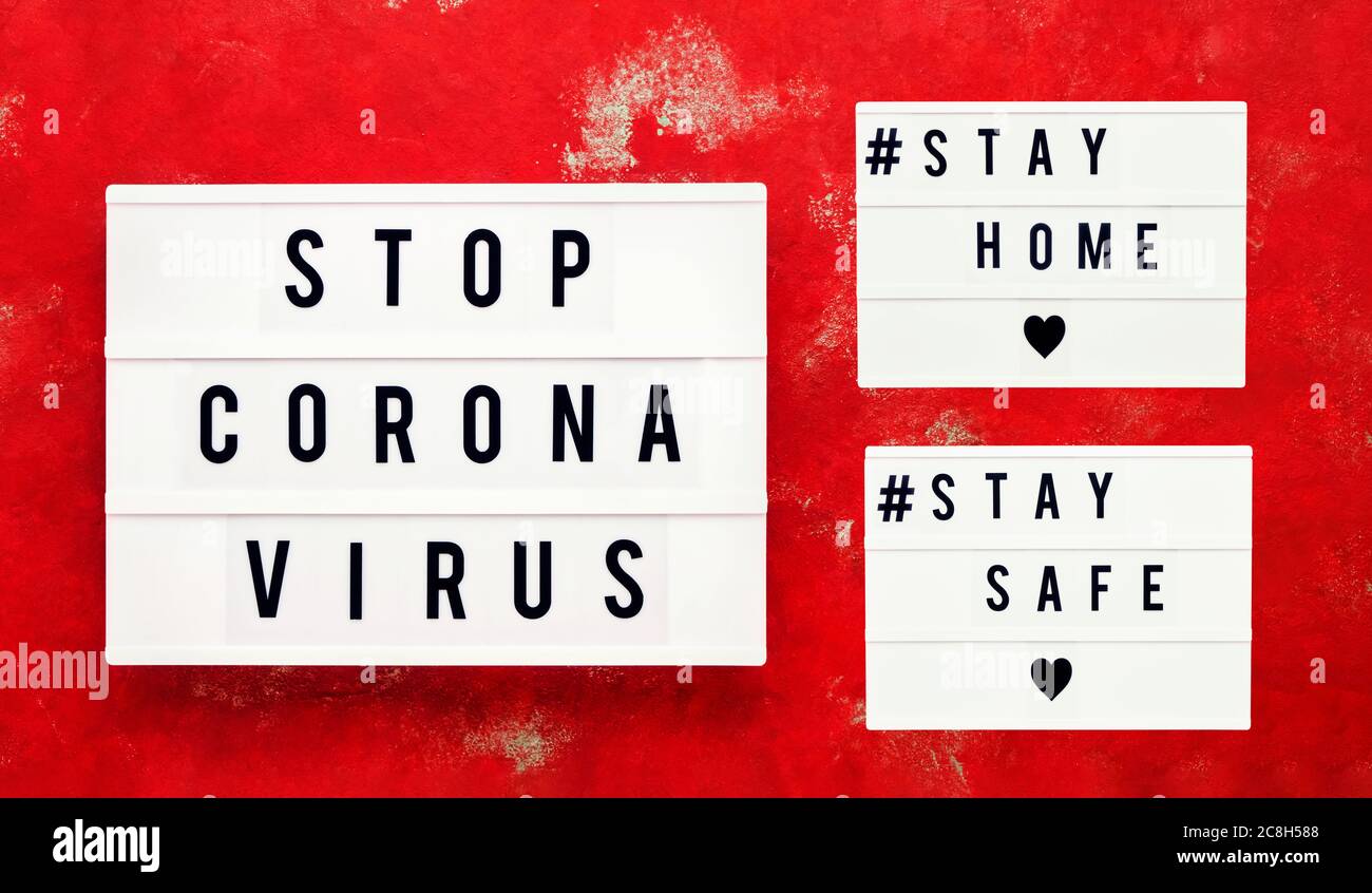 ARRESTARE IL VIRUS CORONA, RIMANERE A CASA e STARE AL SICURO scritto in una scatola luminosa su sfondo rosso brillante. Concetto sanitario e medico. Vista dall'alto. Concetto di quarantena Foto Stock