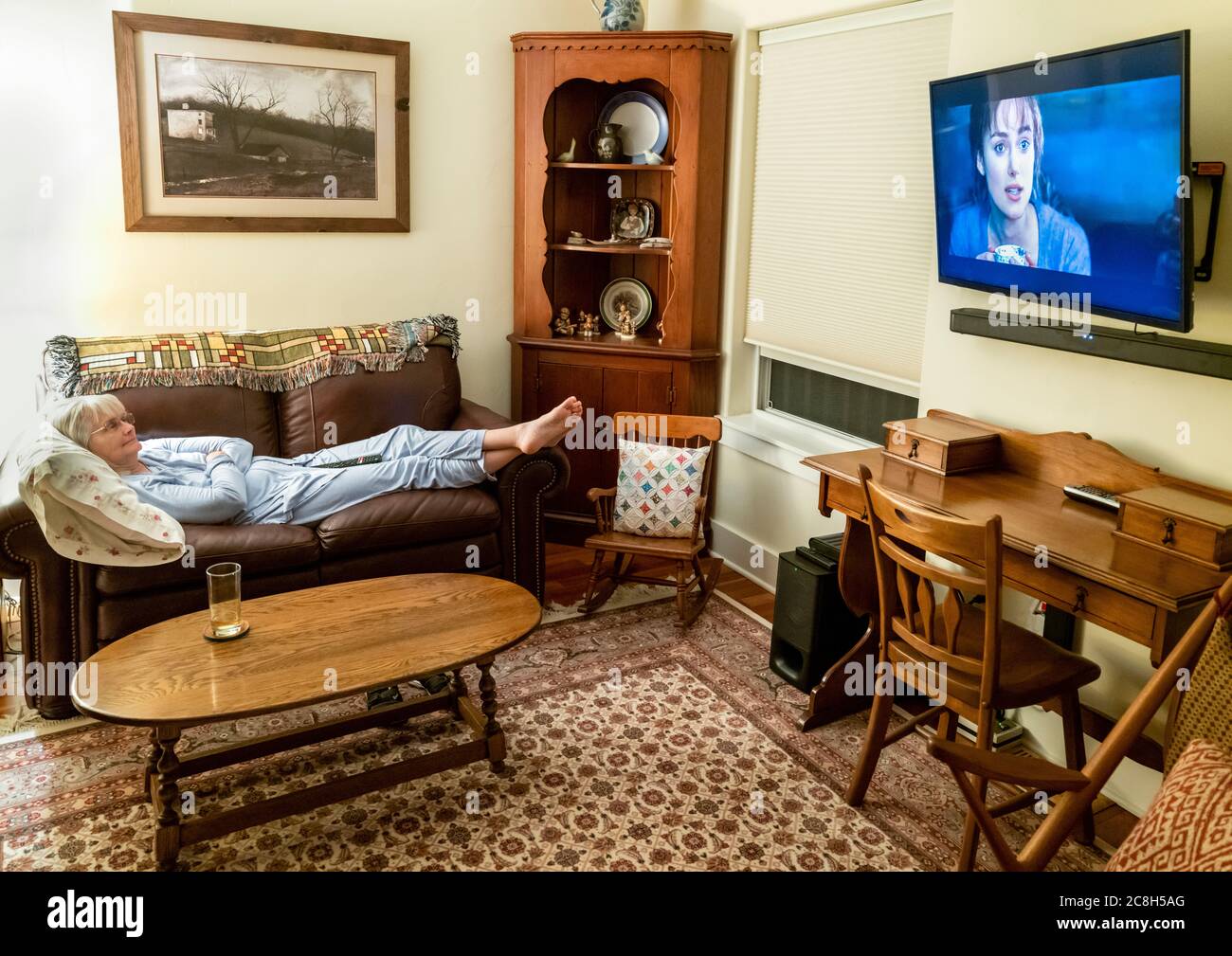 Donna anziana si è reclinata sul divano rilassandosi e guardando la televisione a grande schermo Foto Stock