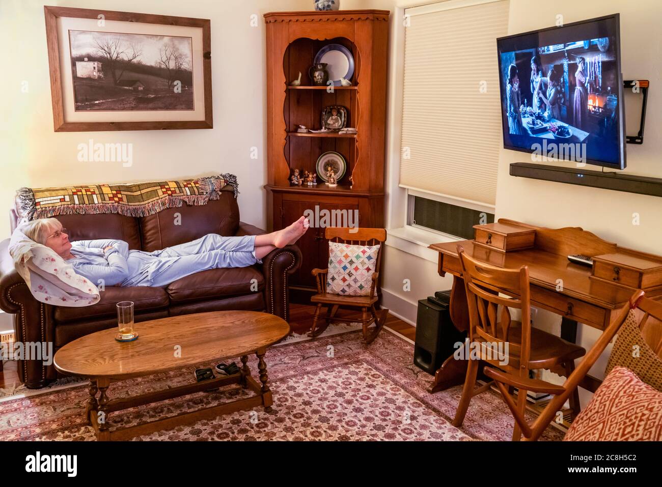 Donna anziana si è reclinata sul divano rilassandosi e guardando la televisione a grande schermo Foto Stock