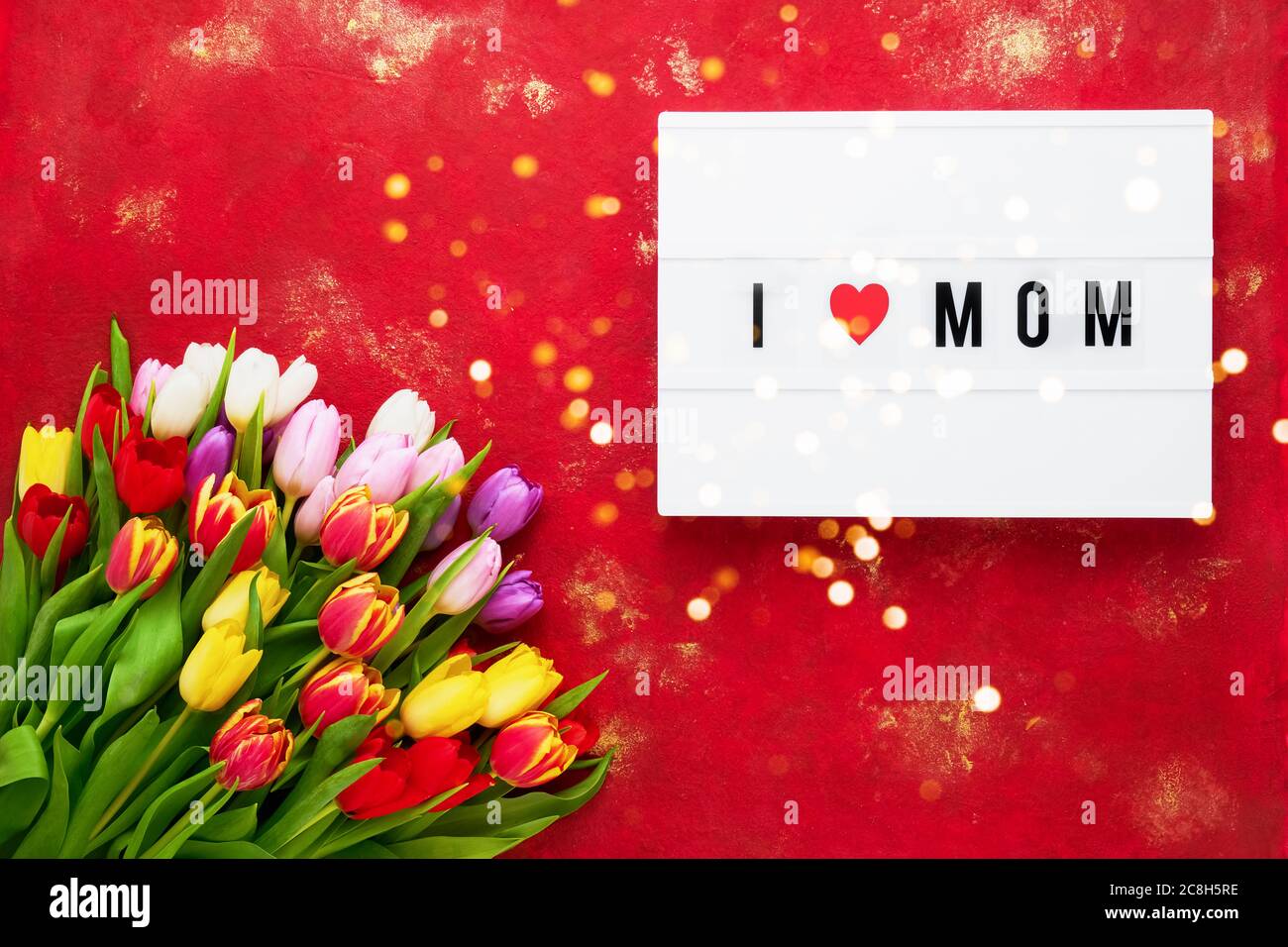 Biglietto d'auguri per il giorno della mamma. Colorato tulipani bouquet su sfondo rosso e mi PIACE MOM scritto su scatola luce. Concetto di celebrazione del giorno della mamma. Vista dall'alto, Foto Stock