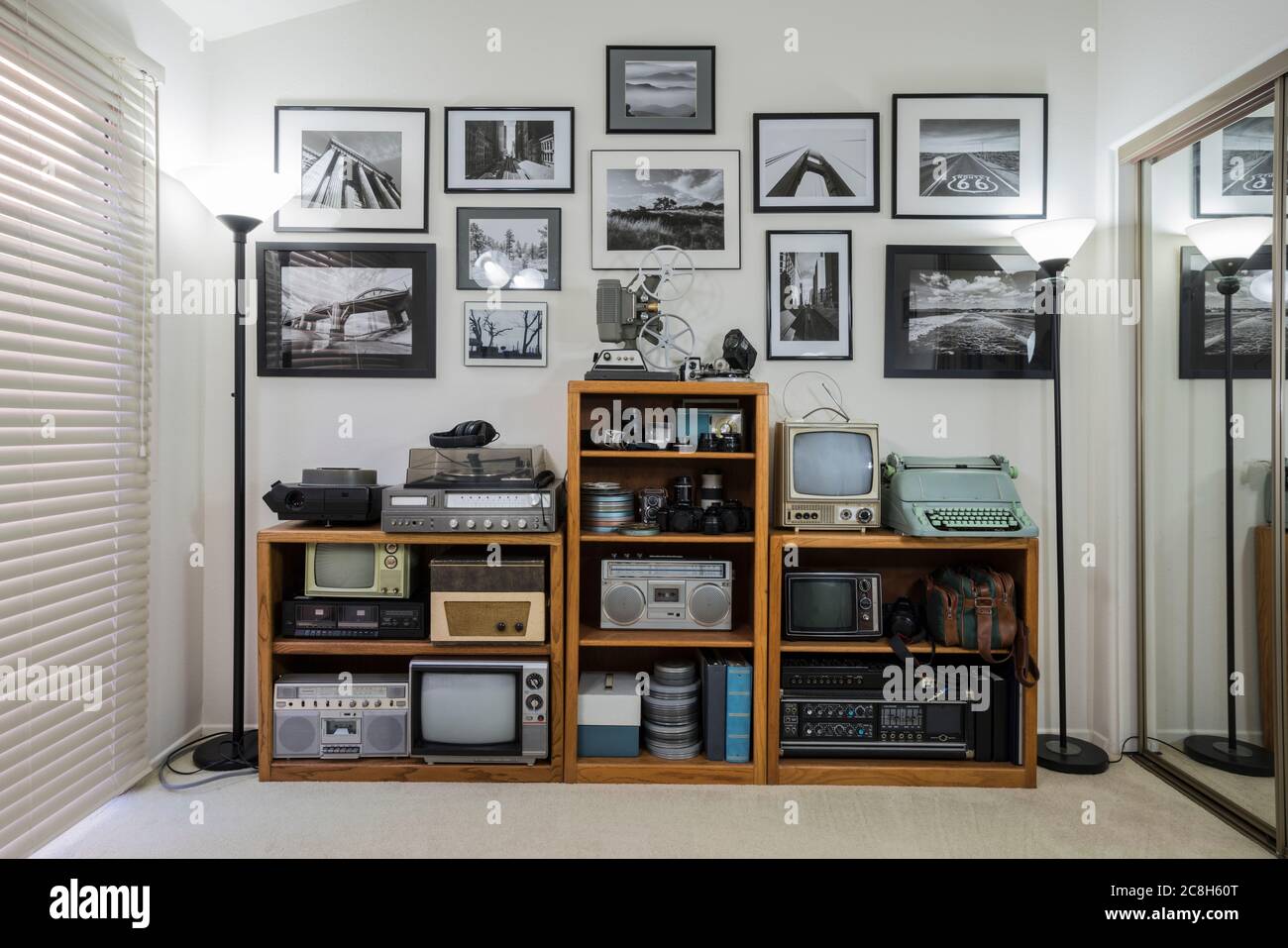 Mensole Bric-a-brac con elettronica vintage da collezione e foto in bianco e nero incorniciate in un piccolo ufficio domestico. Wall art è il lavoro dei fotografi. Foto Stock