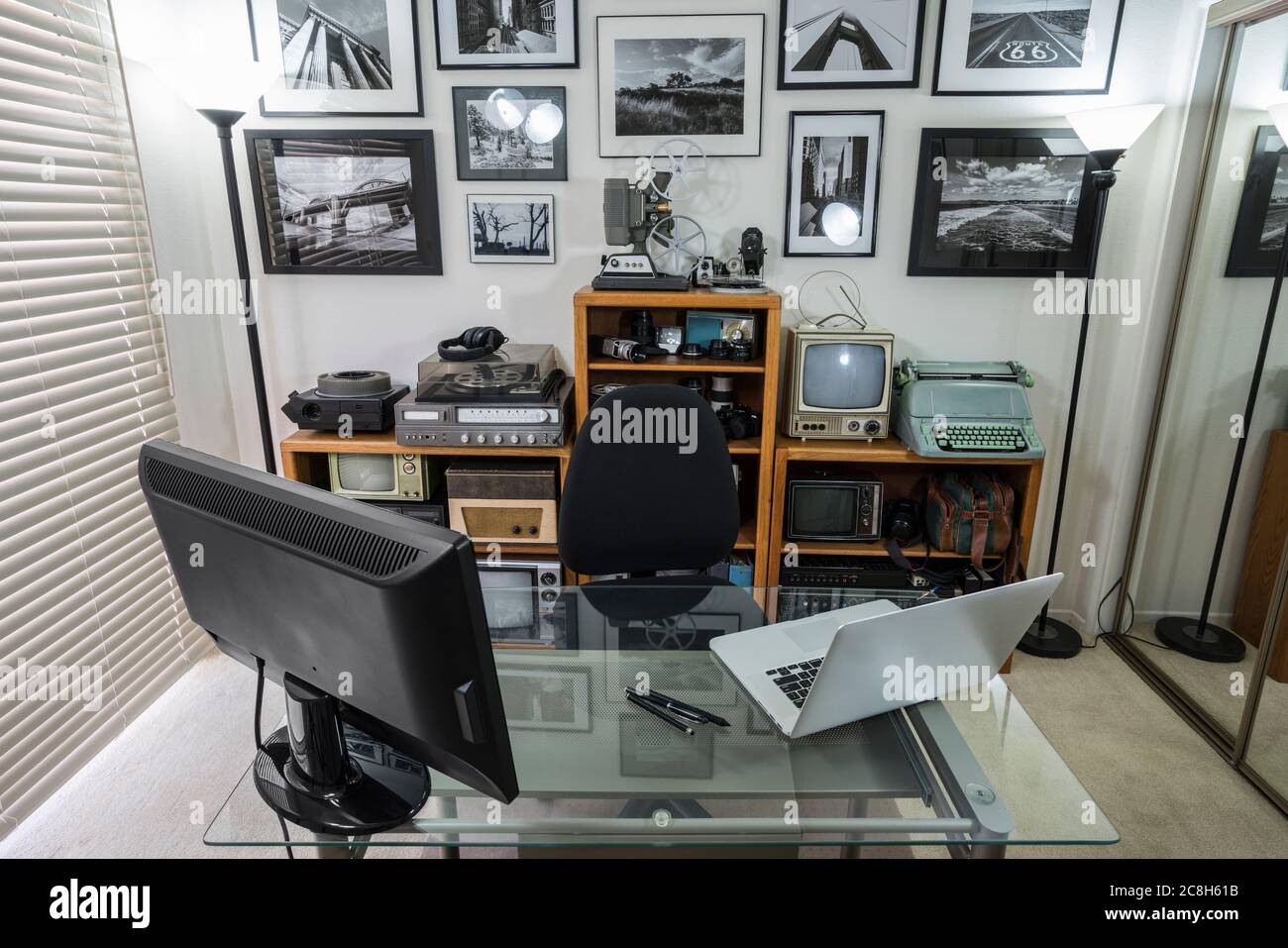 Home Office con oggetti da collezione elettronici vintage sugli scaffali e foto in bianco e nero incorniciate sulla parete. L'arte della parete è il lavoro dei phtotographers. Foto Stock