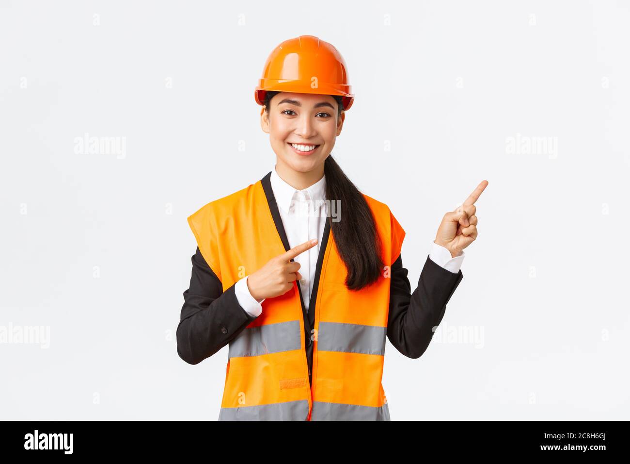 Costruzione, costruzione e concetto industriale. Sorridente ingegnere asiatico in casco di sicurezza e abbigliamento riflettente mostrando oggetto, puntando le dita Foto Stock
