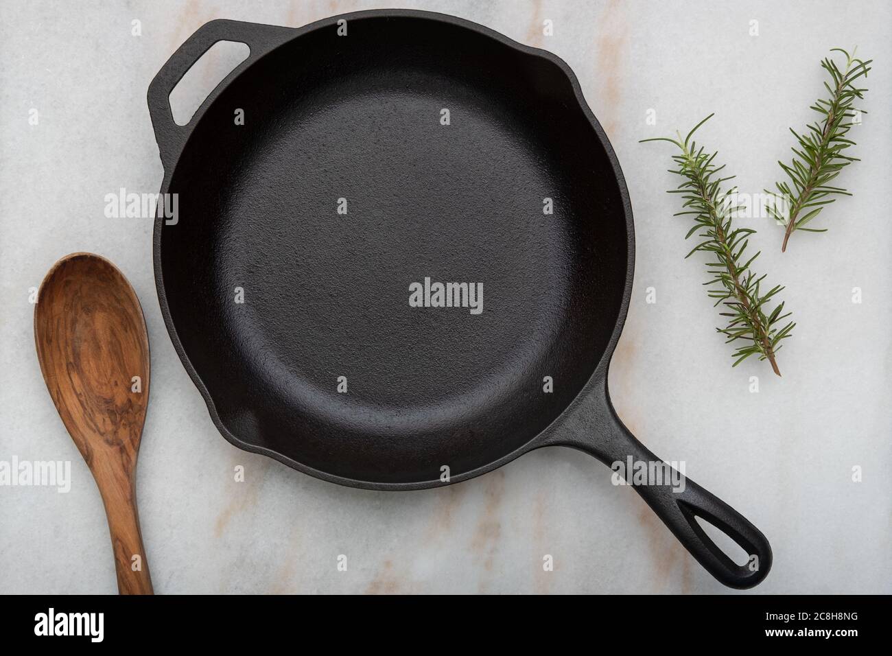 Padella in ghisa con cucchiaio su fondo bianco con rametti di rosmarino Foto Stock