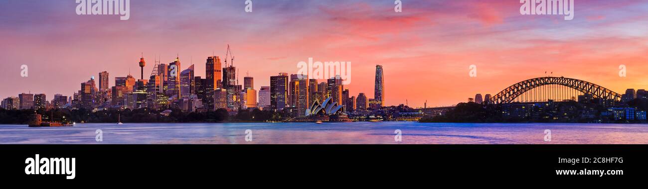 Tramonto arancione rosso sullo skyline cty di Sydney attraverso il porto in un ampio panorama. Foto Stock