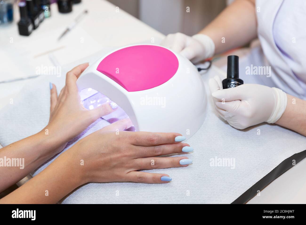 Primo piano bella donna mani e lampada per unghie sul tavolo. Salone gel unghie. Lampada UV. Processo di essiccazione del gel sulle unghie. Bellezza e cura di sé. Tecnologia moderna Foto Stock