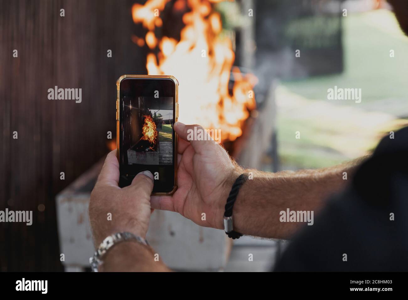 Uomo che scatta una foto del barbecue con il suo cellulare. Picnic. Primo piano. L'uomo adulto sta scattando le foto del fuoco sul suo smartphone il giorno di sole. BA Foto Stock