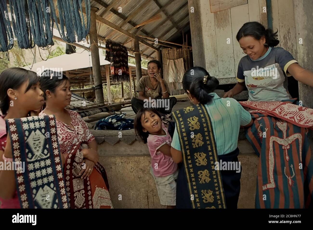 Donne che espongono tessuti ai visitatori di Umabara, Pau, Isola di Sumba, Indonesia. La tessitura è una tradizionale fonte alternativa di reddito per gli abitanti di un villaggio nell'isola secca di Sumba, Indonesia. Foto Stock