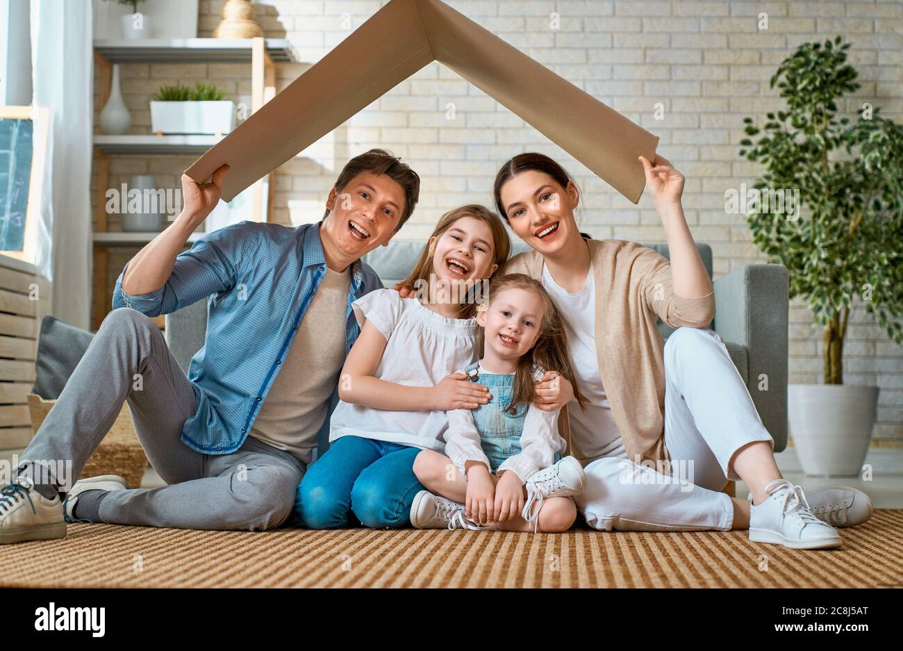 Madre, padre e bambine in camera con il simbolo del tetto. Concetto di alloggio per la famiglia giovane. Foto Stock