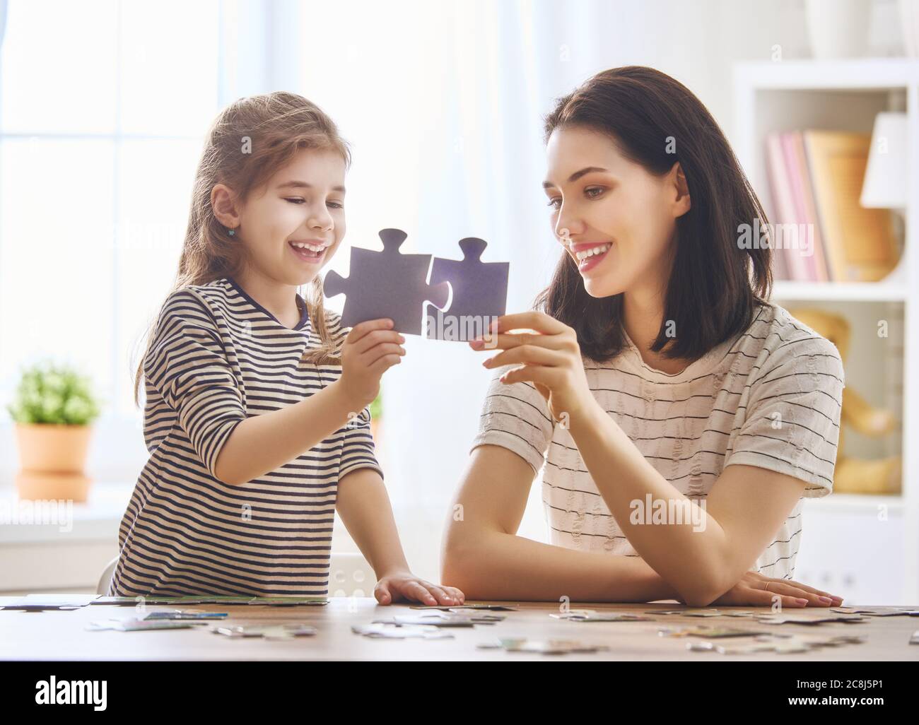 Buona famiglia. Madre e figlia fanno insieme puzzle. La donna adulta insegna al bambino di risolvere i puzzle. Foto Stock