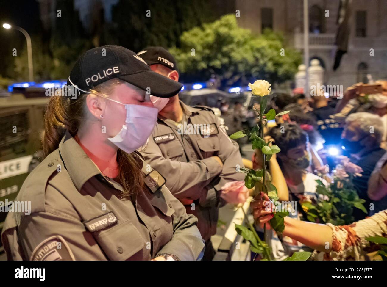 I manifestanti danno fiori alla polizia mentre migliaia di manifestanti massacrati fuori dalla residenza ufficiale del primo ministro Benjamin Netanyahu a Gerusalemme, chiedono le sue dimissioni per le sue accuse di corruzione e ciò che chiamano cattiva gestione della crisi del coronavirus e danneggiano la democrazia a Gerusalemme, Israele. Foto Stock