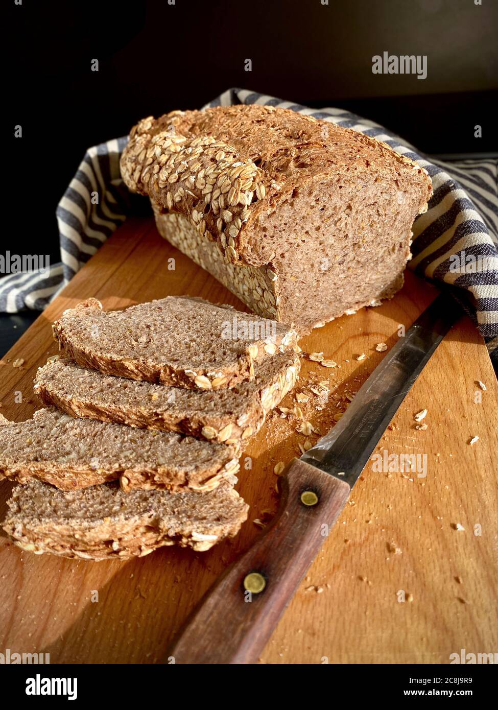 Pane tradizionale tedesco di pane multiverale Vollkornbrot, parzialmente tagliato a fette su un tagliere di legno, coltello con manico di legno. Naturale Foto Stock