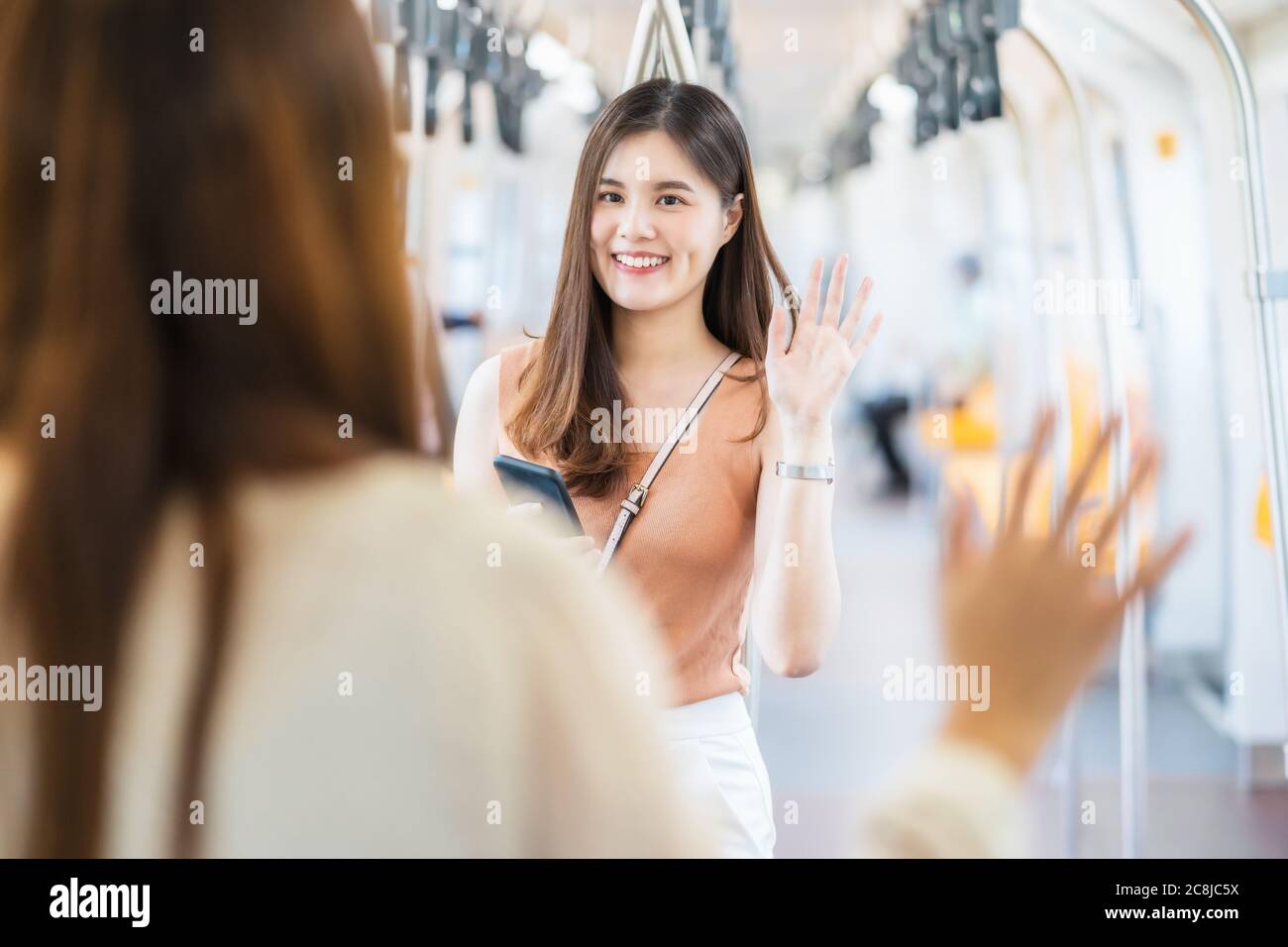 Giovane donna asiatica passeggero che indossa maschera chirurgica e la mano ondeggiante per il saluto al suo amico in treno della metropolitana quando si viaggia in grande città a Covid19 fuori Foto Stock Giovane donna asiatica passeggero che indossa maschera chirurgica e la mano ondeggiante per il saluto al suo amico in treno della metropolitana quando si viaggia in grande città a Covid19 fuori Foto Stock
