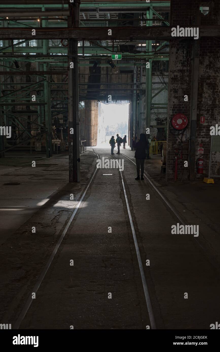 La luce si riversa attraverso un'ampia porta di officina, riflette le vecchie linee ferroviarie e le silhouette delle persone sulla Cockatoo Island nel porto di Sydney, Australia Foto Stock