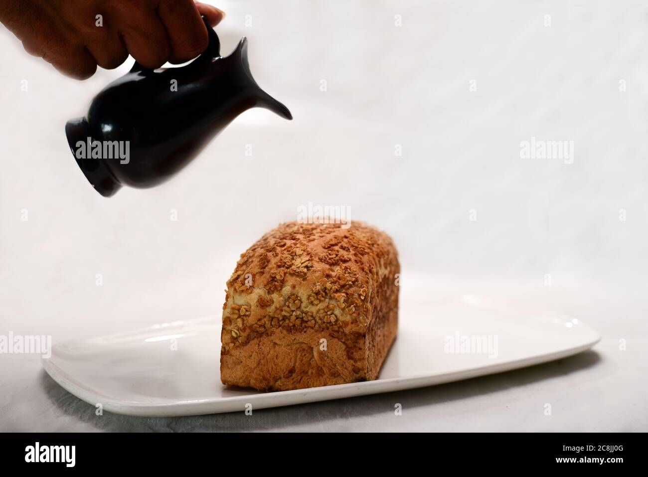 vaso nero in mano e pane su piastra bianca isolato su sfondo bianco. Foto Stock