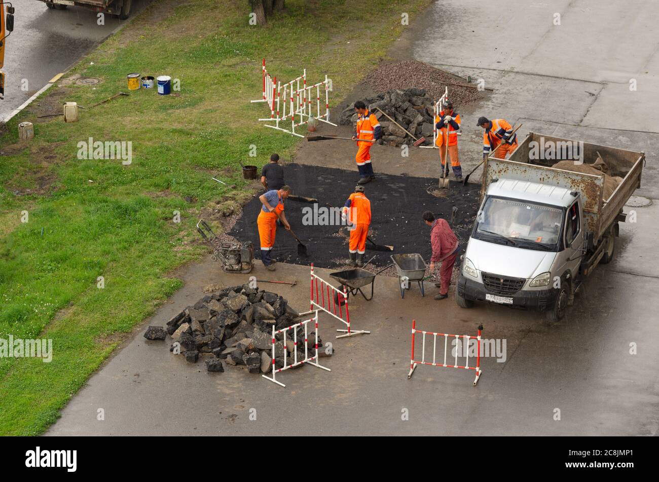 San Pietroburgo, Russia - 28 luglio 2019: Squadra di lavoratori in tute arancioni stende asfalto sul marciapiede in condizioni di pioggia Foto Stock