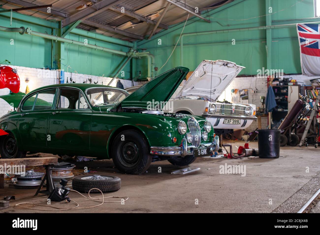 Jaguar Mk2 berlina e Ford Cortina in piedi con i loro cofani rialzati in una classica officina di restauro auto, con pneumatici, ruote e attrezzi intorno a loro Foto Stock