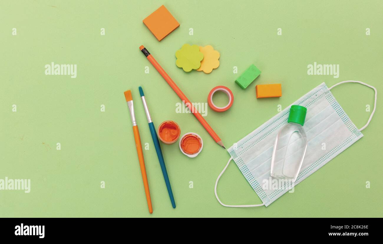 Misure di prevenzione della diffusione del coronavirus a scuola. Maschera medica, gel di disinfezione delle mani con alcool e forniture scolastiche su sfondo color verde pastello, top Foto Stock