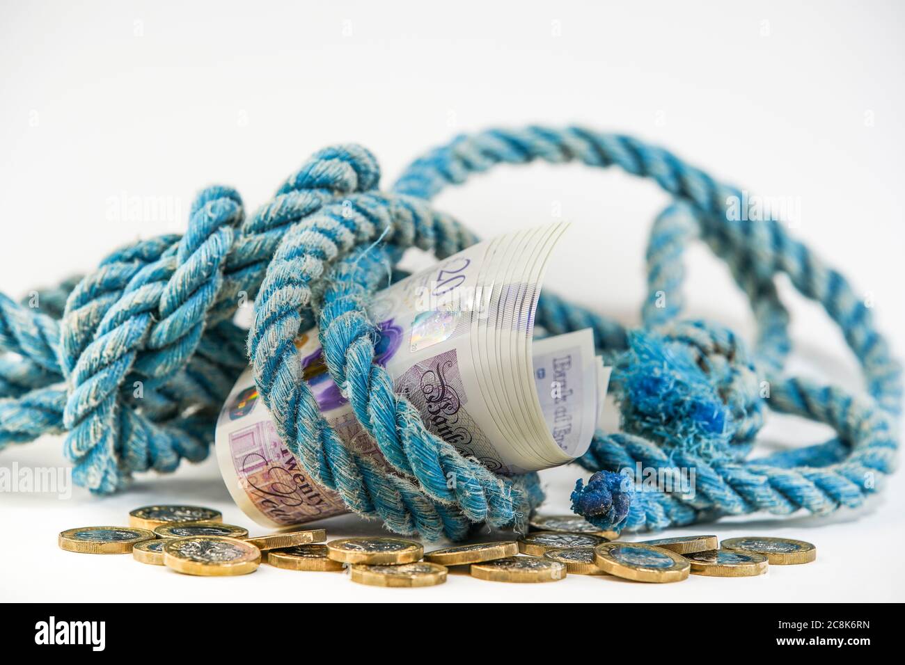 Primo piano di un fascio di 20 £note avvolto in vecchia corda su pila di cambio sciolto, con sfondo bianco. Concetto, metafora: Soldi per la vecchia corda. Foto Stock