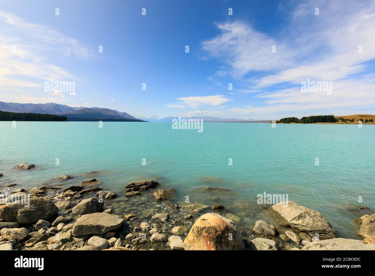 Le rocce sul litorale del turchese, glaciale, Lago Pukaki con il Monte Cook e le Alpi meridionali sullo sfondo. Foto Stock