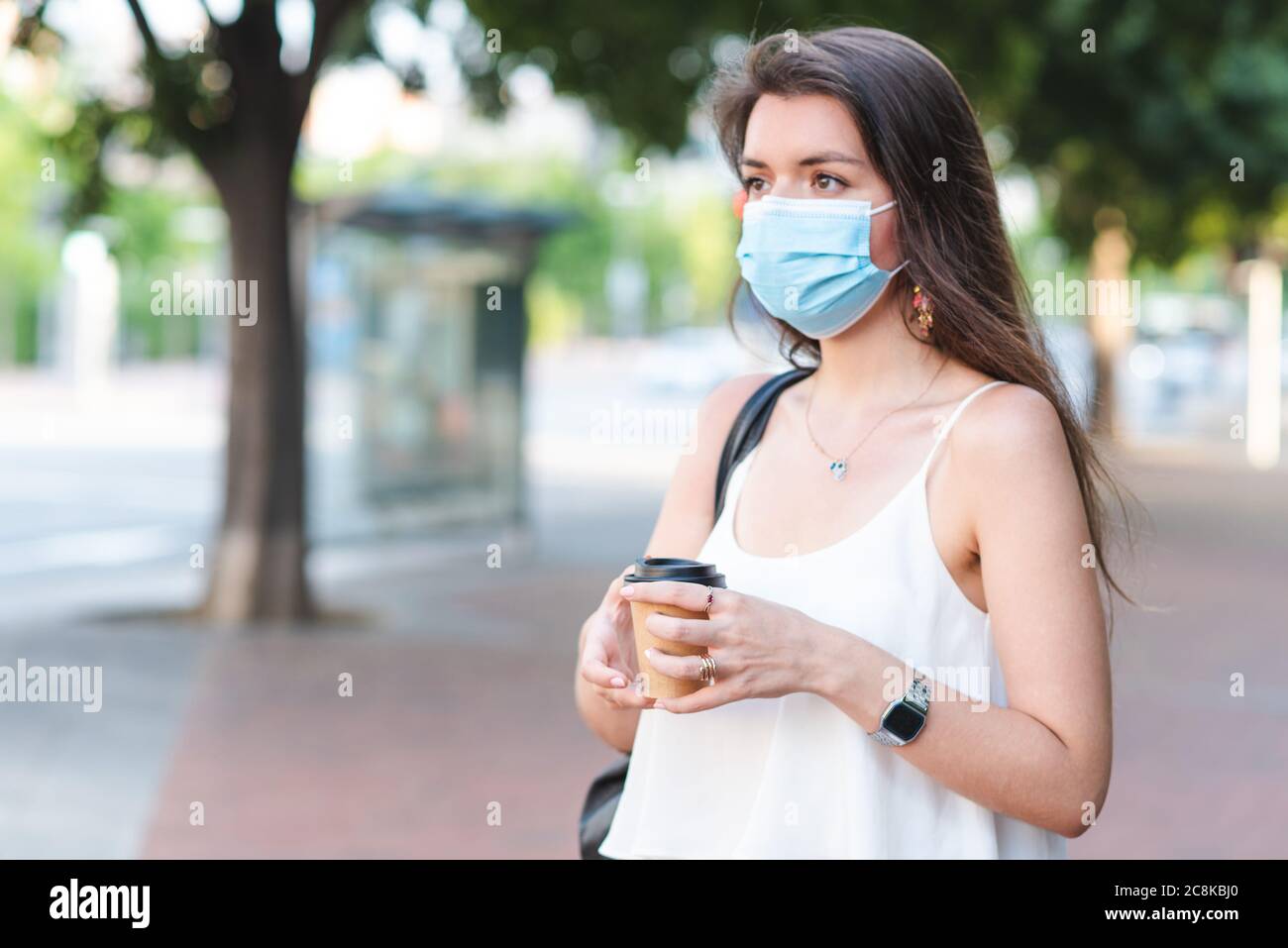 tazzina da togliere il caffè sulle mani di una giovane donna caucasica con maschera chirurgica. fuoco selettivo sulla tazza Foto Stock