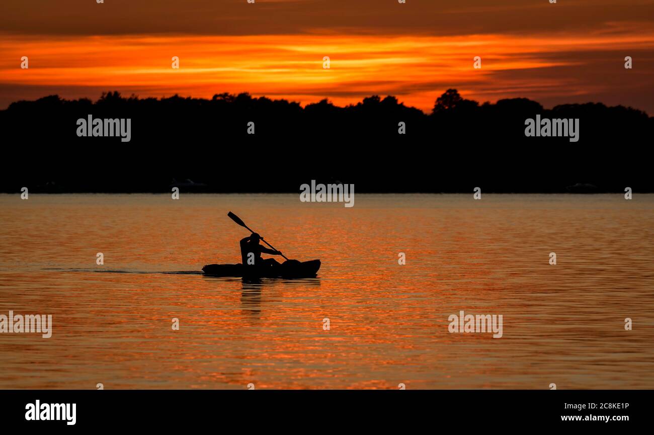 Kayak Lone con silhouette contro il tramonto arancione Foto Stock