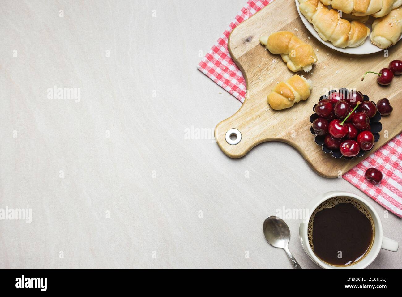 Colazione con croissant fatti in casa, caffè e ciliegie dolci su sfondo chiaro e testurizzato, vista dall'alto con spazio per la copia. Foto Stock