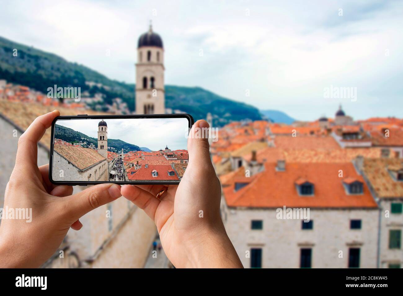 Turista che scatta foto del centro di Dubrovnik. Uomo che tiene il telefono e scattare foto dei tetti rossi dalle mura della città di Dubrovnik Foto Stock