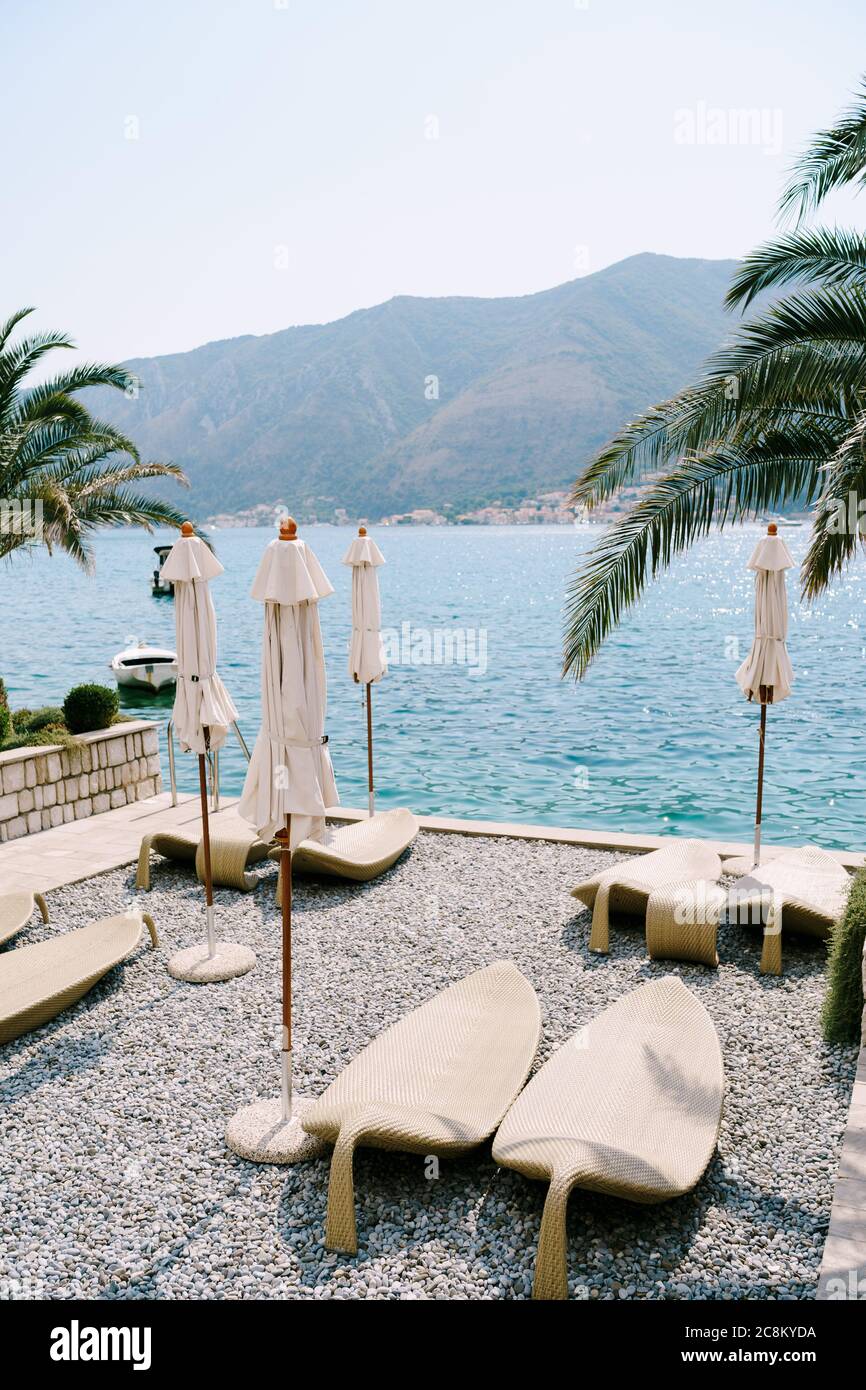 Lettini in plastica sulla spiaggia di ciottoli. Kotor Bay in Montenegro, la città di Dobrota. Sotto i rami di palmi di data. Foto Stock