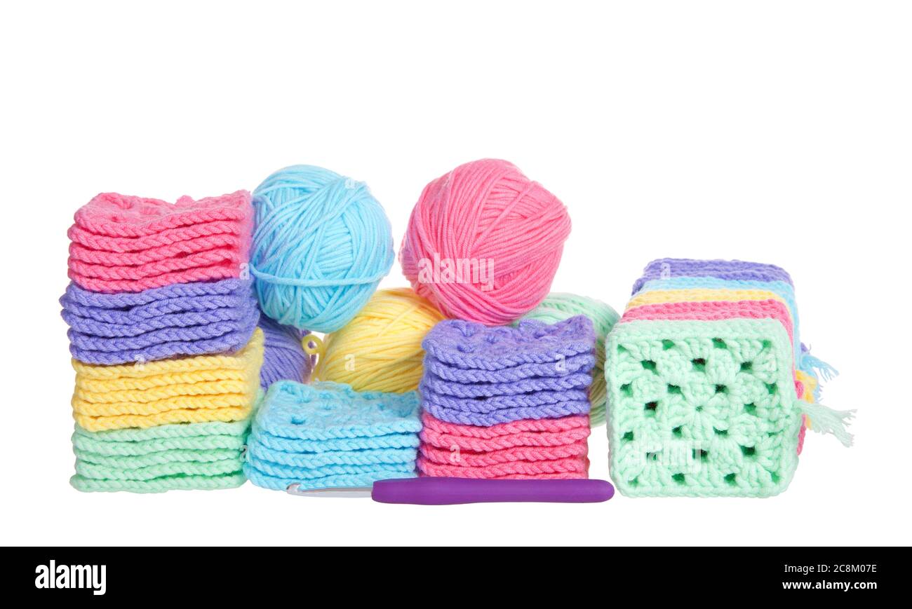 Pile di colorate quadratini granny crochet mano con palle di filato accatastate dietro, uncino a uncinetto che si posa davanti. Isolato su sfondo bianco. Foto Stock