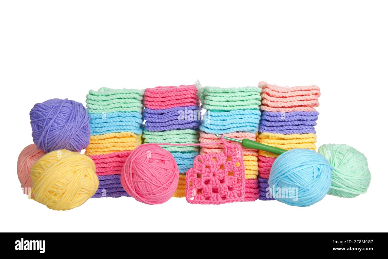 Pile di colorate quadratini granny a crochet con palle di filato accatastate dietro, uncino a crochet che si posa davanti con quadrato di granata parzialmente completato. È Foto Stock