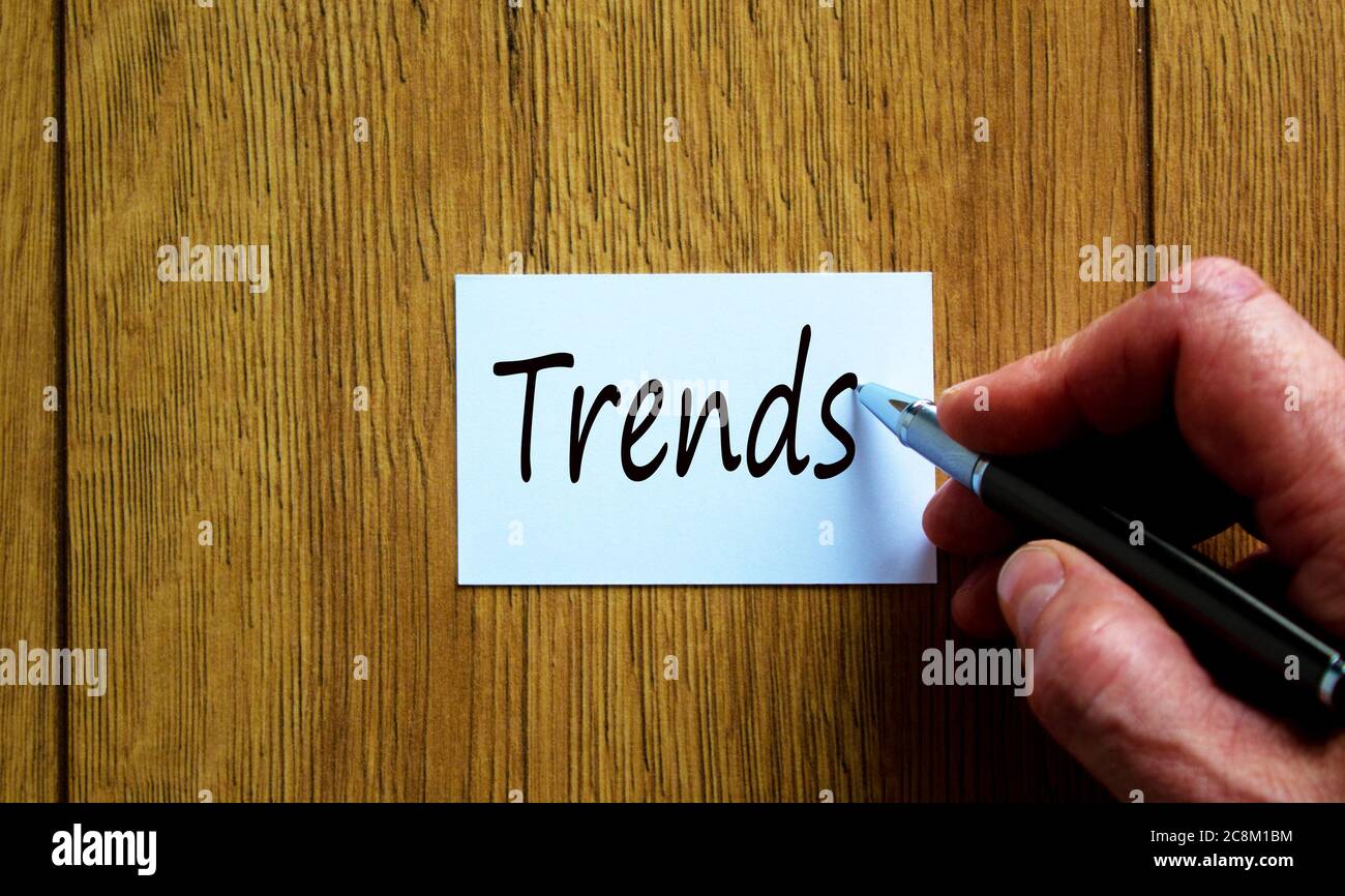 Mano maschile scrivendo 'Trends' su nota bianca, isolato su sfondo di legno. Foto Stock