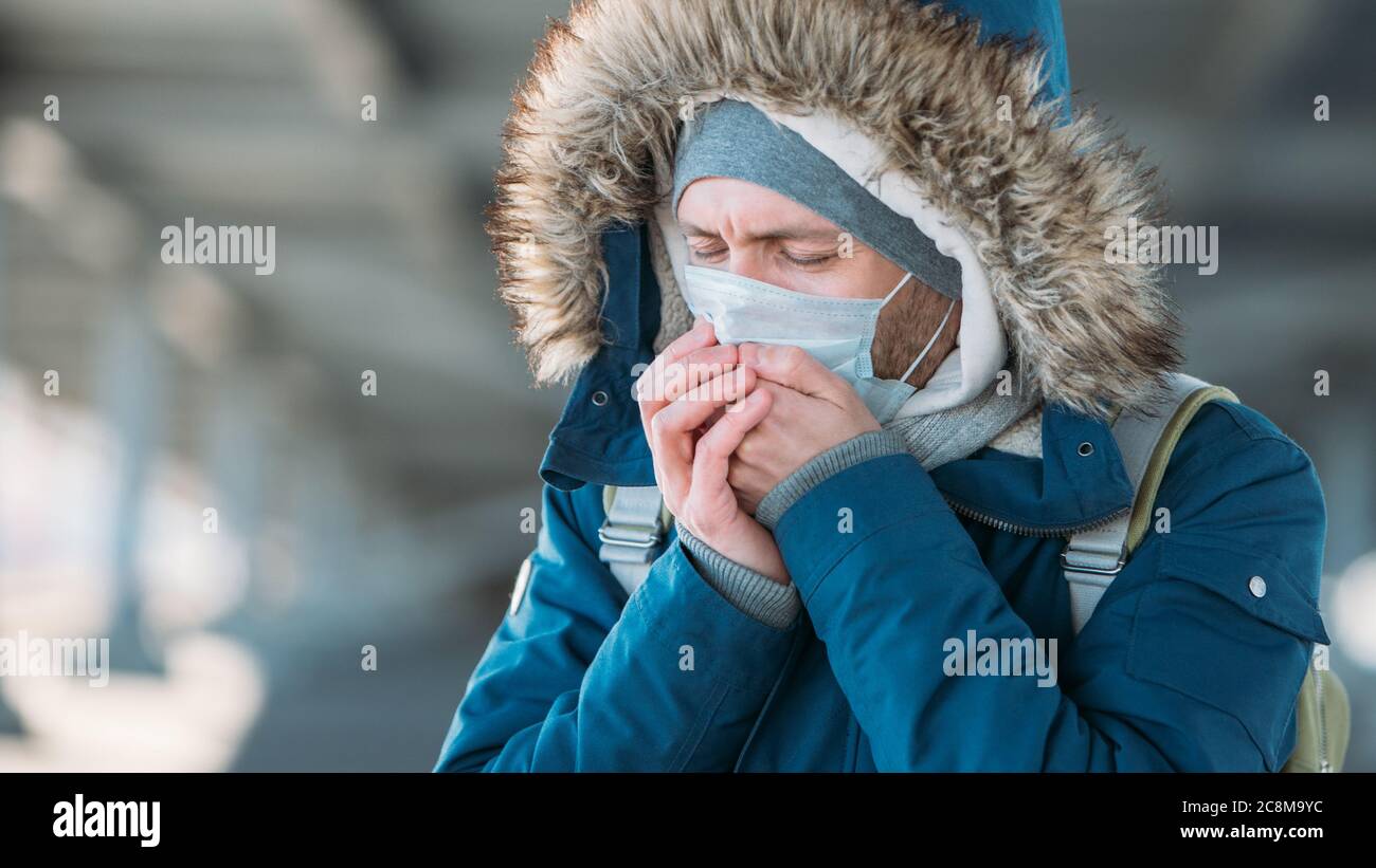 Primo piano di un giovane malato che ha un freddo, starnuti, tosse e indossare maschera medica viso, all'aperto. Bronchite, malattia, epidemia di influenza Foto Stock