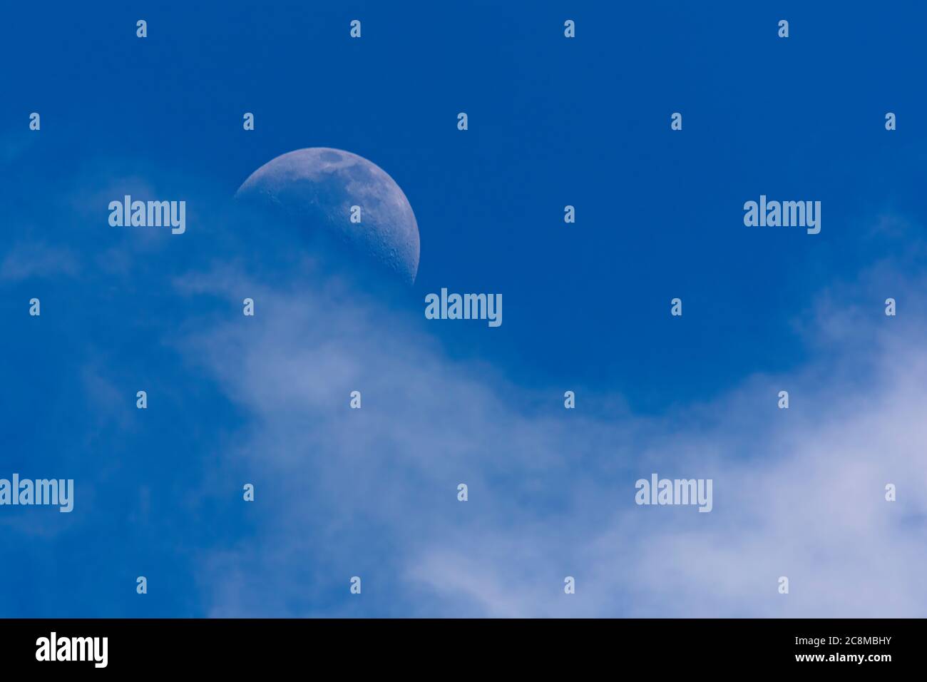 Mezza luna nascosta tra le nuvole nel bel mezzo del pomeriggio senza che il sole crolca Foto Stock