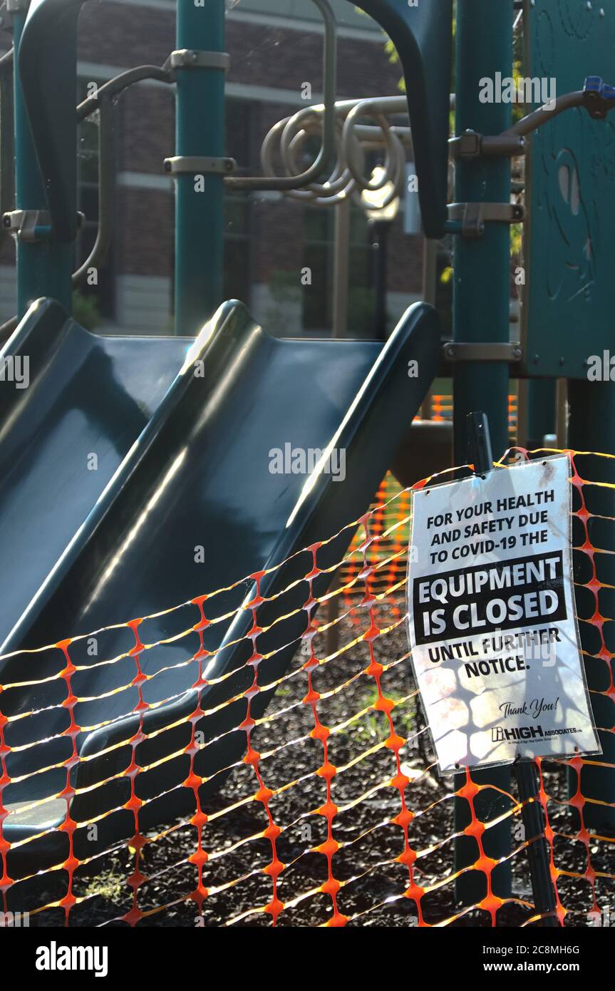 Un cartello e una recinzione arancione in plastica intorno a un parco giochi per bambini, un cartello con la scritta "l'attrezzatura è chiusa fino a nuovo avviso", a causa della pandemia del COVID-19 Foto Stock