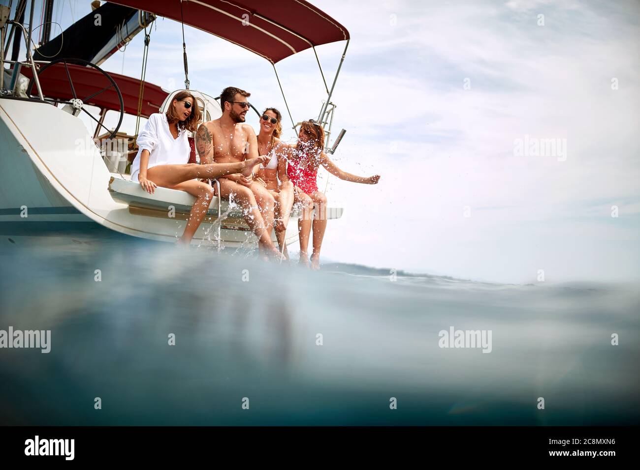 Amici che si rilassano a poppa di uno yacht e raffreddando le gambe in acqua Foto Stock