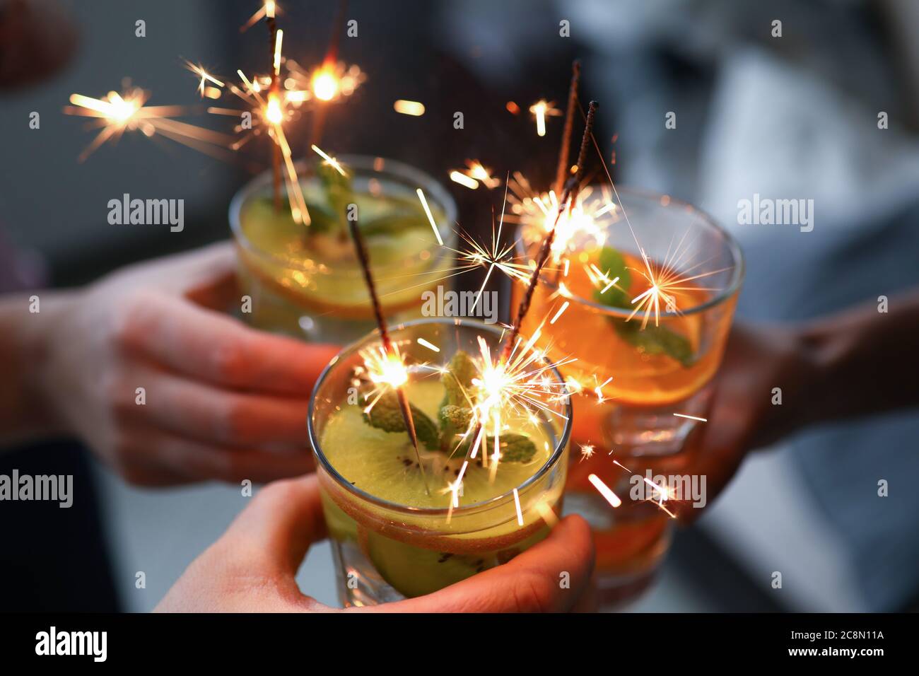 Tre mani tengono tre bicchieri con cocktail e sparklers primo piano. Foto Stock