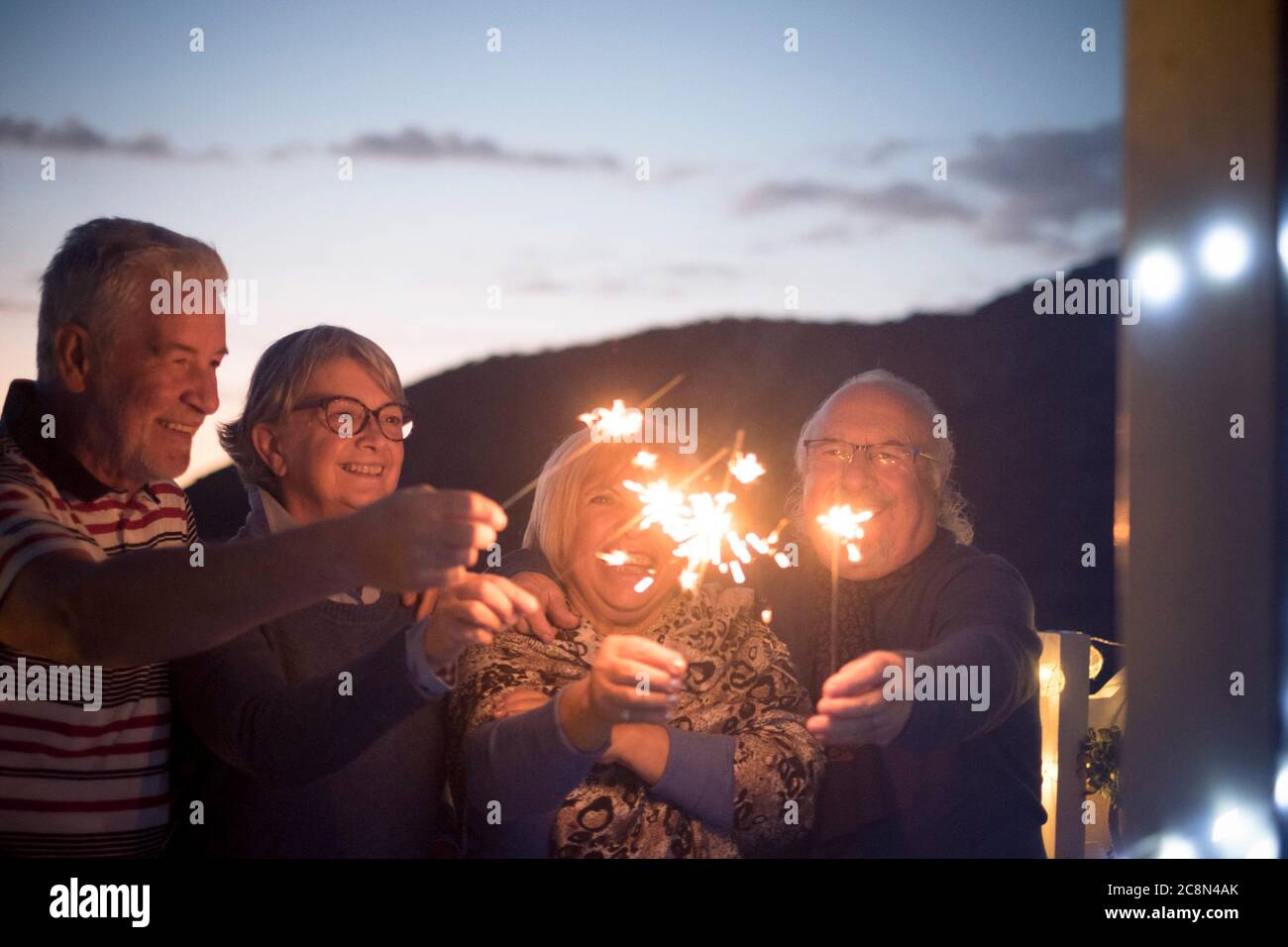 Gli amici anziani della gente hanno divertimento e festeggiano di notte con sparkler del fuoco - concetto di nuovo anno di vigilia e le coppie anziane maturi godono di amicizia a. Foto Stock