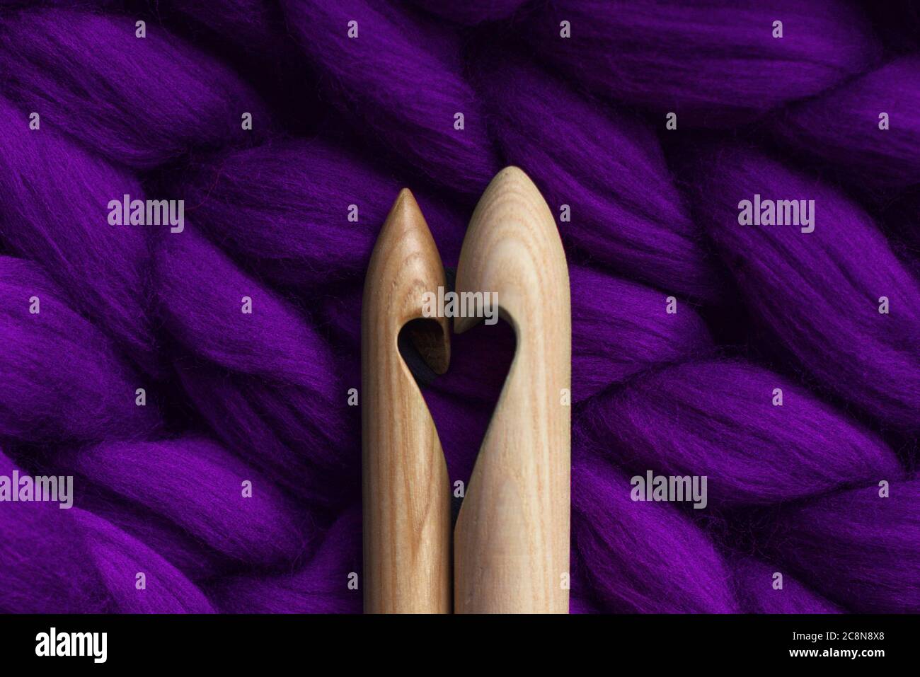 Due aghi da maglieria con taglio a forma di cuore, giacenti su una lana merino, fatti a mano, viola Foto Stock